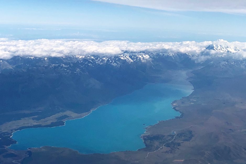 South Island. A view from a plane flying over the Southern Alps, turquoise blue Lake Pukaki and Mt Cook in the background, shrouded in cloud.