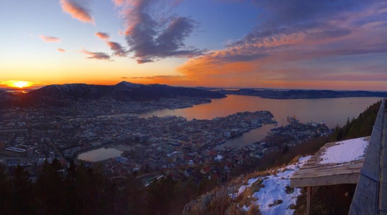 travel when not travelling - sunset over Bergen in Norway - orange streaked sky with the city below dark next to the water.