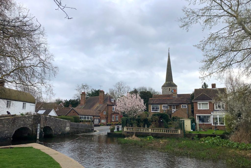 Eynsford village, with a church steeple, pretty brick houses and a bridge crossing a river.