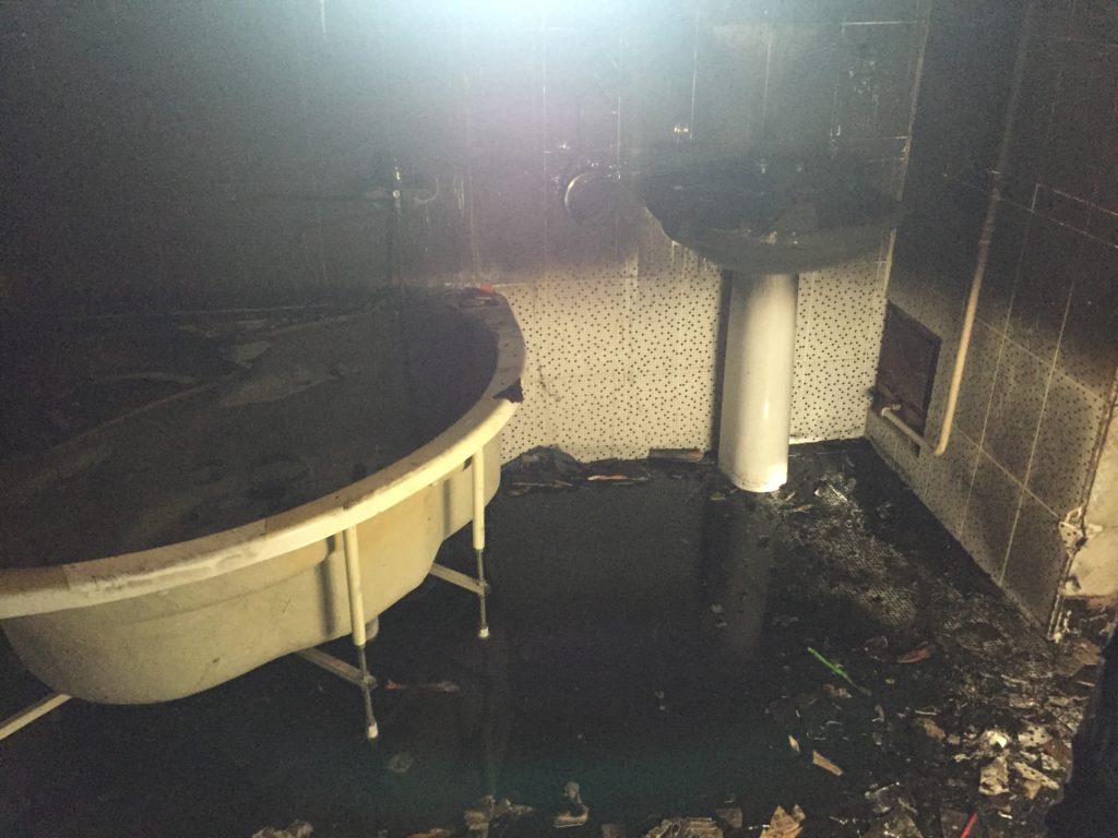 Fire in Samarkand - the bathroom completely burnt out after the fire, with water on the floor and black walls.