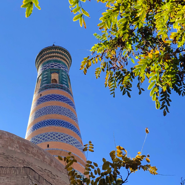 October 2019 - looking up at a minaret, with a bright blue sky and green leaves.