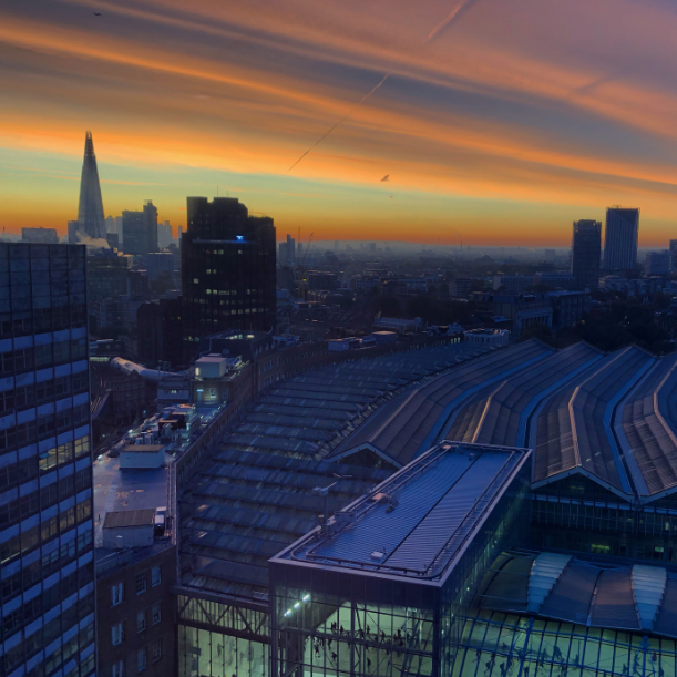 A streaky sunset in December 2019 with the Shard in the background and Waterloo train station roof in the foreground. The sunset is orange and red in the sky.