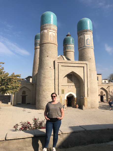 Budget Uzbekistan - a photo of Bethen wearing a stripey t-shirt and jeans and standing in front of Chor Minor. A small castle like structure with four domed turrets.
