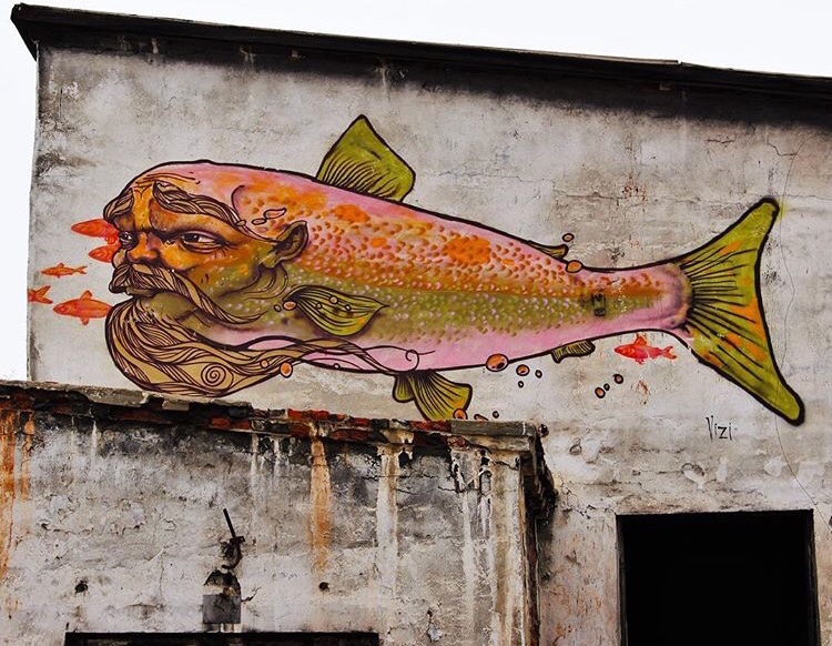 Street art on Olkhon Island. A white painted concrete wall, adorned with a painting of a fish with a man's head, with a long flowing beard.