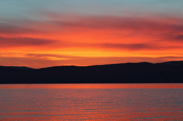 Sunset on Olkhon Island. The sky is  awash with oranges and reds, reflected by the water. The hills are black silhouettes. 