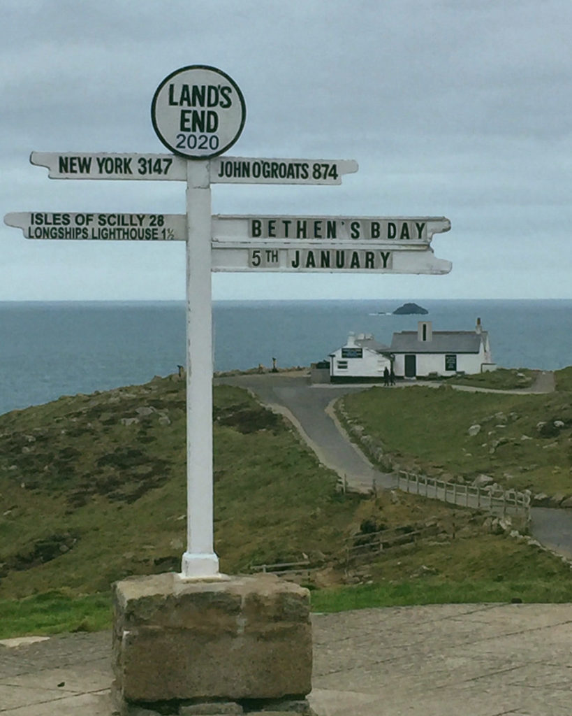 A view from the top of Land's End, including the legendary sign post and a look down towards the sea and the cliff edge.