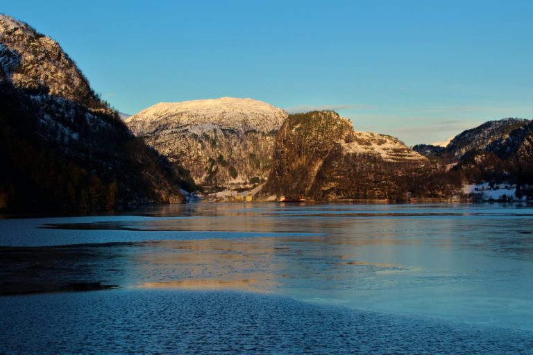 First light touches the snow covered slopes in the background, which come down to the fjord which is covered in a thin layer of sea ice.