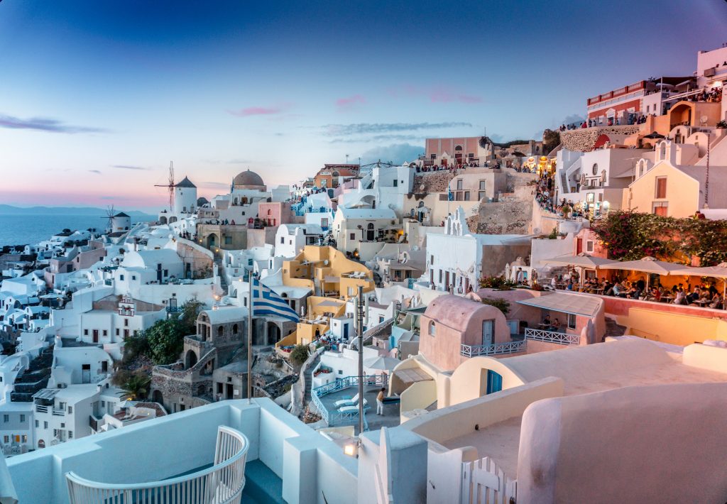 Bucket list. Santorini in Greece. A photo taken at dusk, with white buildings rising up a slope, crowded on top of one another.