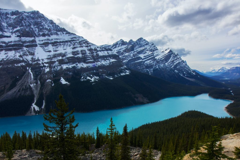 bucket list long distance hikes - the Canadian Rockies. A sweeping landscape photo of mountains covered in snow with a turquoise blue lake and a pine forest more to the forefront.