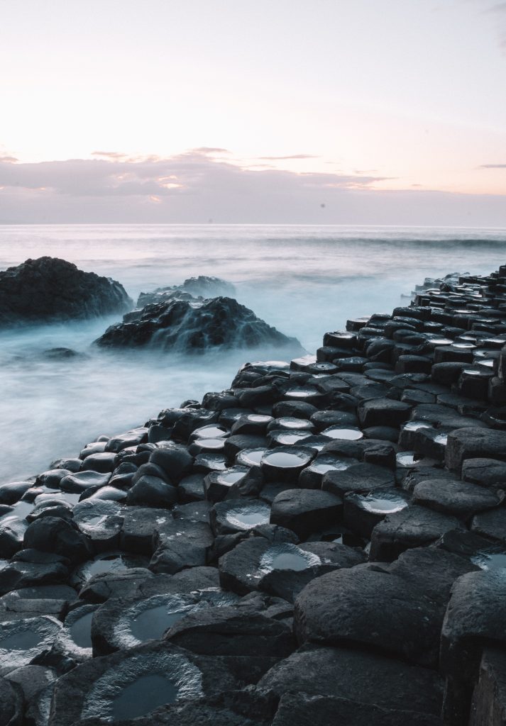 Giant's Causeway in Ireland. A picture of some of the hexagonal rock formations in the foreground, with the sea and waves crashing over them in the background.