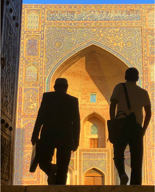 Bucket list. Kalyan Mosque in Bukhara, Uzbekistan. Two men are silhouetted against the backdrop of a colourful facade as they climb steps to exit the mosque.