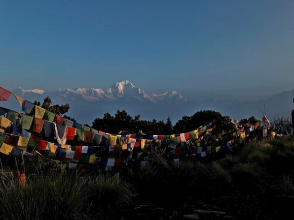 Bucket list. The Annapurna mountains in Nepal. Multi-coloured prayer flags strung up in the foreground, with the outlined snow capped mountain peaks rising from the mist in the background.