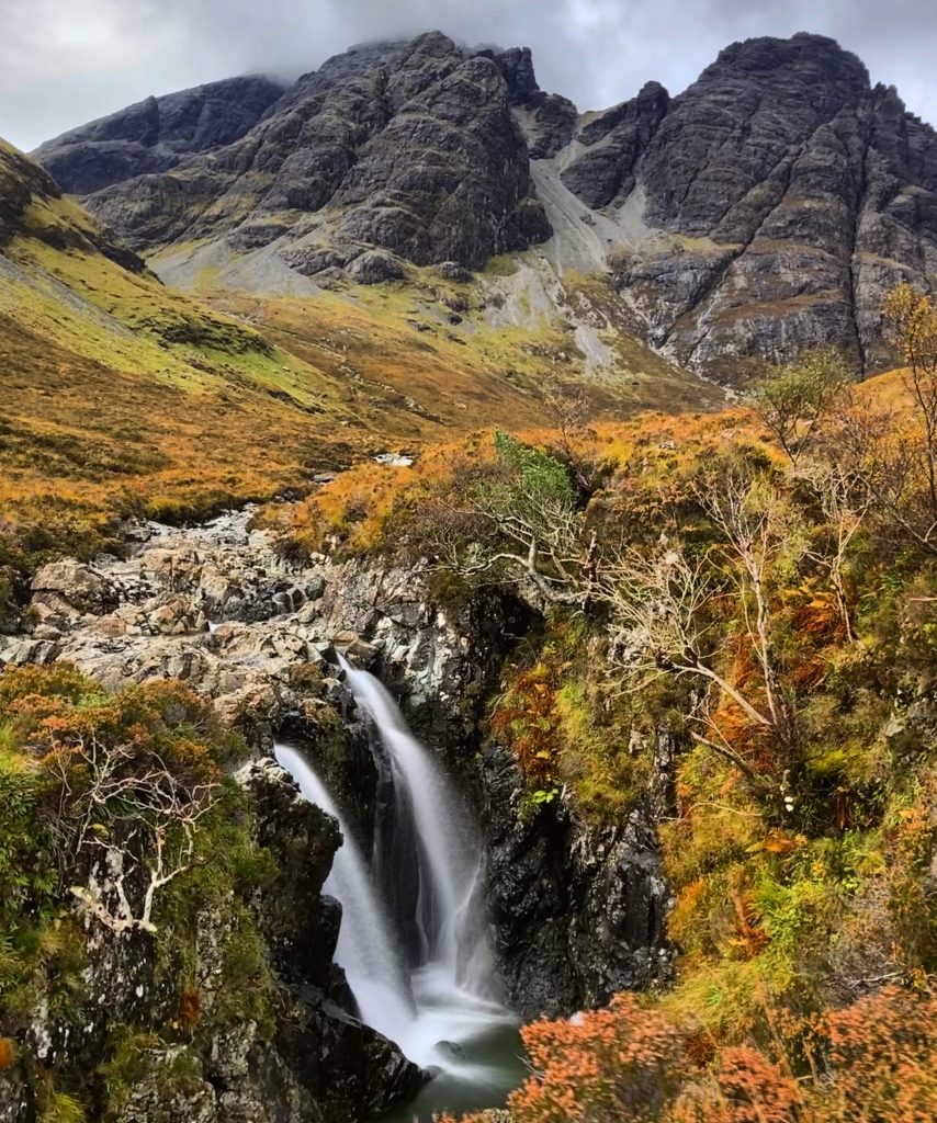 A waterfall on Skye, with autumnal hues and a mountain in the background.